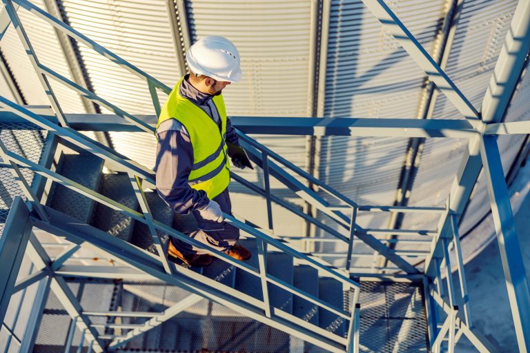 An industry worker descending the stairs on silo with tablet in hands.